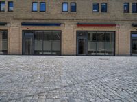 the sidewalk is paved with stones and has a bench in front of it, with no people inside