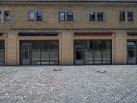 the sidewalk is paved with stones and has a bench in front of it, with no people inside