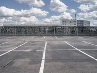 an empty parking lot with a fence around it and several buildings in the background of this image