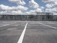 an empty parking lot with a fence around it and several buildings in the background of this image