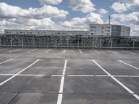an empty parking lot with a fence around it and several buildings in the background of this image