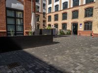 a sidewalk with chairs next to the brick building on the side, some have stairs and some buildings in the background