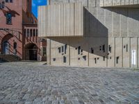 cobblestone driveway surrounded by modern buildings on sunny day with sun reflecting onto the windows