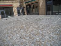 the sidewalk is paved with stones and has a bench in front of it, with no people inside