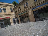 the sidewalk is paved with stones and has a bench in front of it, with no people inside