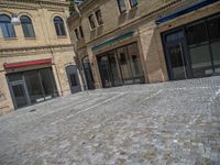 the sidewalk is paved with stones and has a bench in front of it, with no people inside