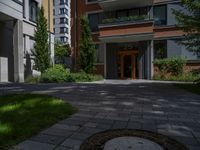 a residential driveway with a bench and bushes in between buildings and green grass on either side