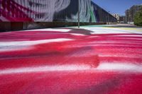 a person with a skateboard walks past a red concrete slab that has a painting of a woman on it