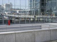 people walking past a train station in an open city square with tall buildings reflected in the windows