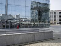 people walking past a train station in an open city square with tall buildings reflected in the windows