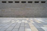 a brick wall next to an empty sidewalk in the afternoon suntime with sunlight reflecting off of windows and squares of tiles