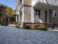 a driveway with an attached walkway and two bikes parked along it on the sidewalk behind a multi - story house