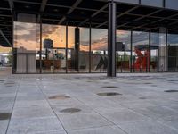 a fire hydrant sitting in front of a glass building under a sunset sky outside