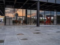 a fire hydrant sitting in front of a glass building under a sunset sky outside