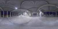 a wide angle view of the inside of an indoor parking lot at night, with multiple windows on each side