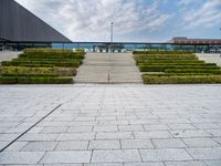 a view of the back steps of a building with shrubs on both sides and two fountains in the background