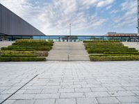 a view of the back steps of a building with shrubs on both sides and two fountains in the background