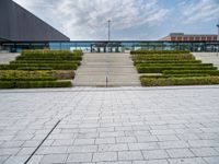 a view of the back steps of a building with shrubs on both sides and two fountains in the background