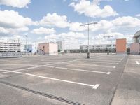 an empty parking lot in a parking lot with two buildings behind it and sky with clouds