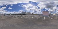 an empty parking lot on a partly cloudy day with a sky background and buildings behind it