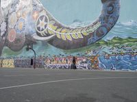 the painted elephant is near a basketball court with a man standing outside of it's door