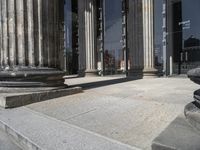 a picture of pillars and one pillar next to a building with many windows and people outside it