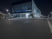 a large building sitting under the city lights at night with an empty road below it