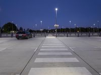 empty parking lot with street lights and poles at dusk, in background are trees and a blue sky
