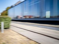 a train passing by some bushes and trees on tracks during the day, while a person holds a phone to her ear