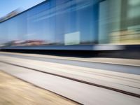 a train passing by some bushes and trees on tracks during the day, while a person holds a phone to her ear