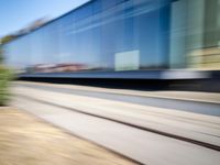 a train passing by some bushes and trees on tracks during the day, while a person holds a phone to her ear