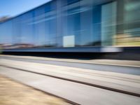 a train passing by some bushes and trees on tracks during the day, while a person holds a phone to her ear