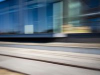 a train passing by some bushes and trees on tracks during the day, while a person holds a phone to her ear