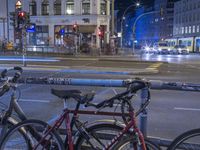 bicycles parked at a rail on a city street at night near buildings and cars parked along a roadway