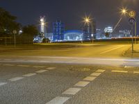 a city at night with lights on and an empty street in the foreground and a blurry picture of cars