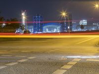 a city at night with lights on and an empty street in the foreground and a blurry picture of cars