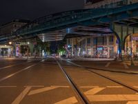 the empty street is filled with people walking and biking under an overpass at night