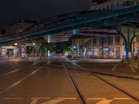 the empty street is filled with people walking and biking under an overpass at night