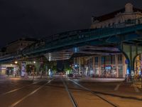 the empty street is filled with people walking and biking under an overpass at night