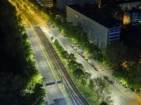 an aerial view of a city at night, with the road and tracks going through the city