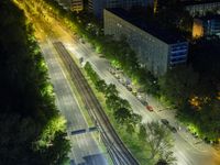 an aerial view of a city at night, with the road and tracks going through the city