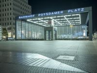 a night time picture of a large building at the bank of potsdam plaza, with light streaming through its glass facade