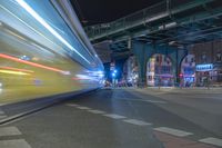 the street lights at night and the bus is turning slowly as it passes underneath a bridge