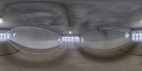 an inside view of two circular mirrors with the lights on in a room with a ceiling of concrete, with large windows