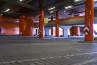 empty, cobblestone street in large underground parking garage area of residential building with orange colored pillars