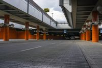 an empty sidewalk and two parked cars under a concrete walkway area, beneath a parking garage