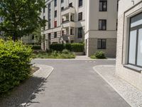 a brick walkway between two beige apartment buildings next to a tree filled street and some bushes