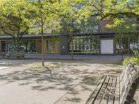 benches in front of a building with trees on it and glass doors to a building