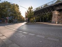 the crosswalk at the street with cars parked on the road below and a bridge overhead