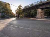 the crosswalk at the street with cars parked on the road below and a bridge overhead